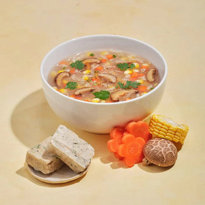 White bowl of shiitake mushroom soup with corn, carrots, and herbs, surrounded by fresh ingredients