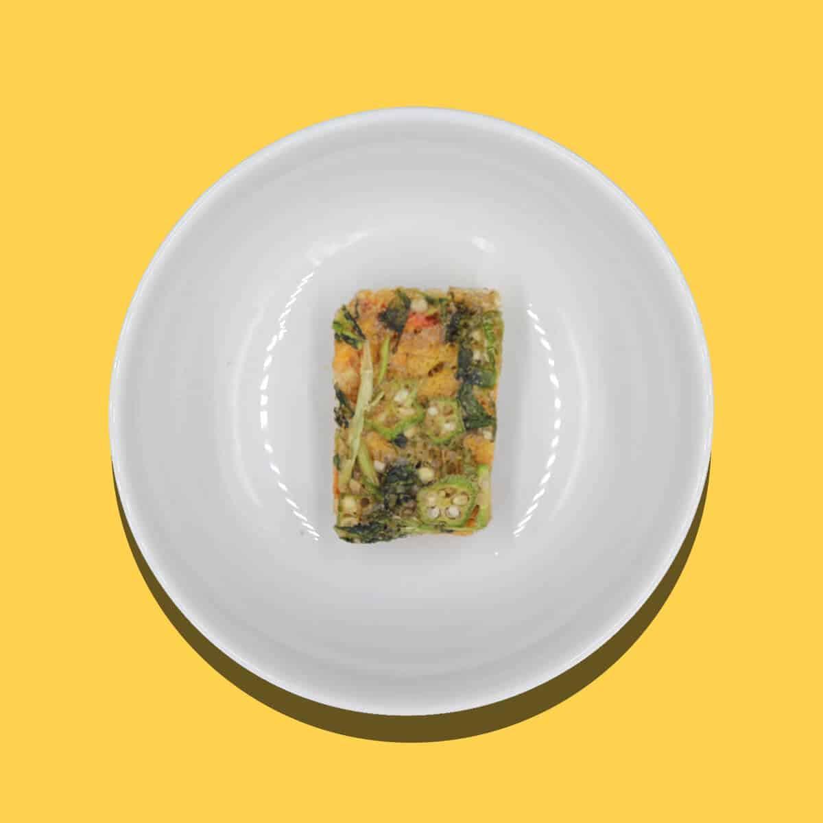 Rectangular sweet and sour block with visible vegetables on white plate against yellow background